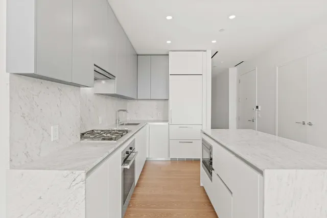a view of an empty room and kitchen with wooden floor