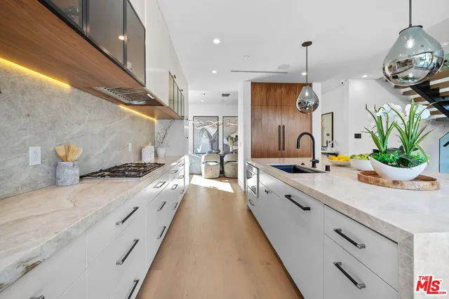 a large kitchen with stainless steel appliances a stove a sink a oven and a dining table with wooden floor