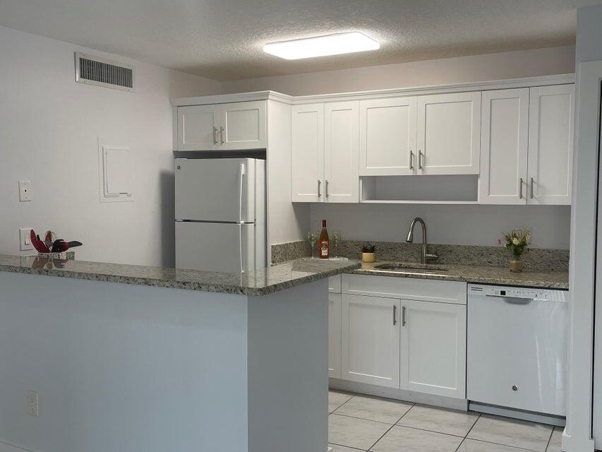 639 Executive Center Drive, Unit O107 West Palm Beach, FL 33401 - Photo 6 of 21 a kitchen with granite countertop white cabinets and refrigerator
