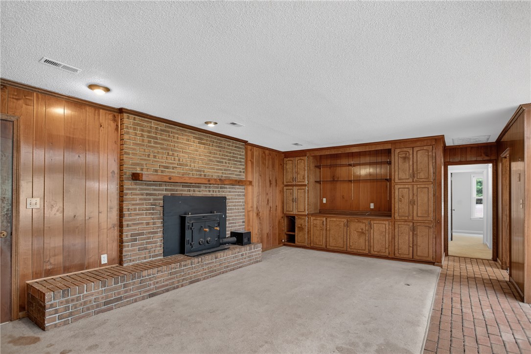 1412 Simpson Road Pendleton, SC 29670 - Photo 11 of 48 A cozy living space features a brick fireplace with an extended hearth, complemented by rich wood paneling and built-in cabinetry.