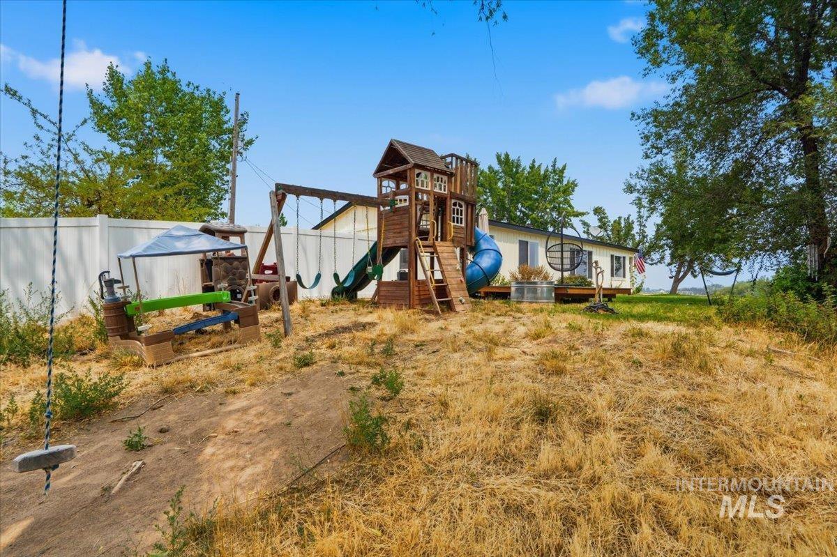 17114 Goodson Road Caldwell, ID 83607 - Photo 36 of 47 Expansive outdoor space featuring a large playset with slides and swings, a white privacy fence, and mature trees