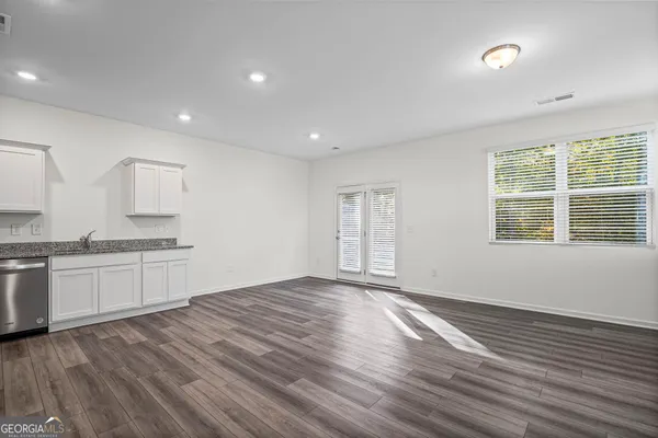 a open kitchen with granite countertop a stove top oven a sink and white cabinets with wooden floor