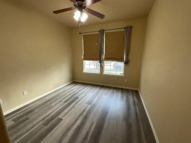 an empty room with wooden floor fan and windows