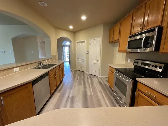 a kitchen with stainless steel appliances granite countertop a sink a stove top oven and wooden floor