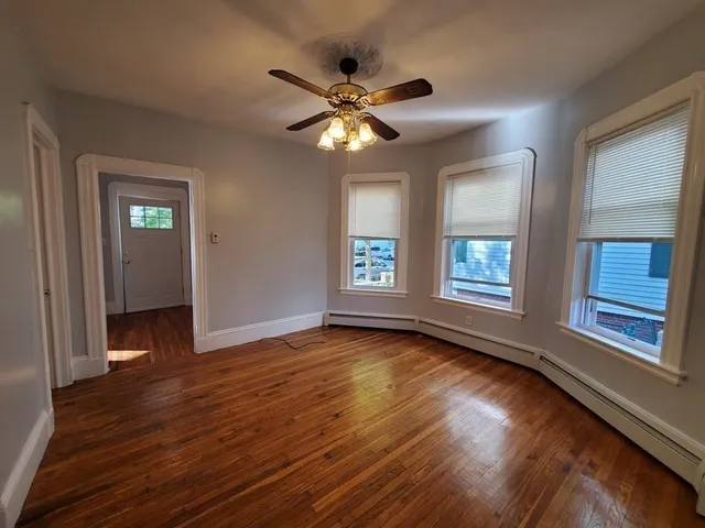 a view of a livingroom with wooden floor a ceiling fan and windows