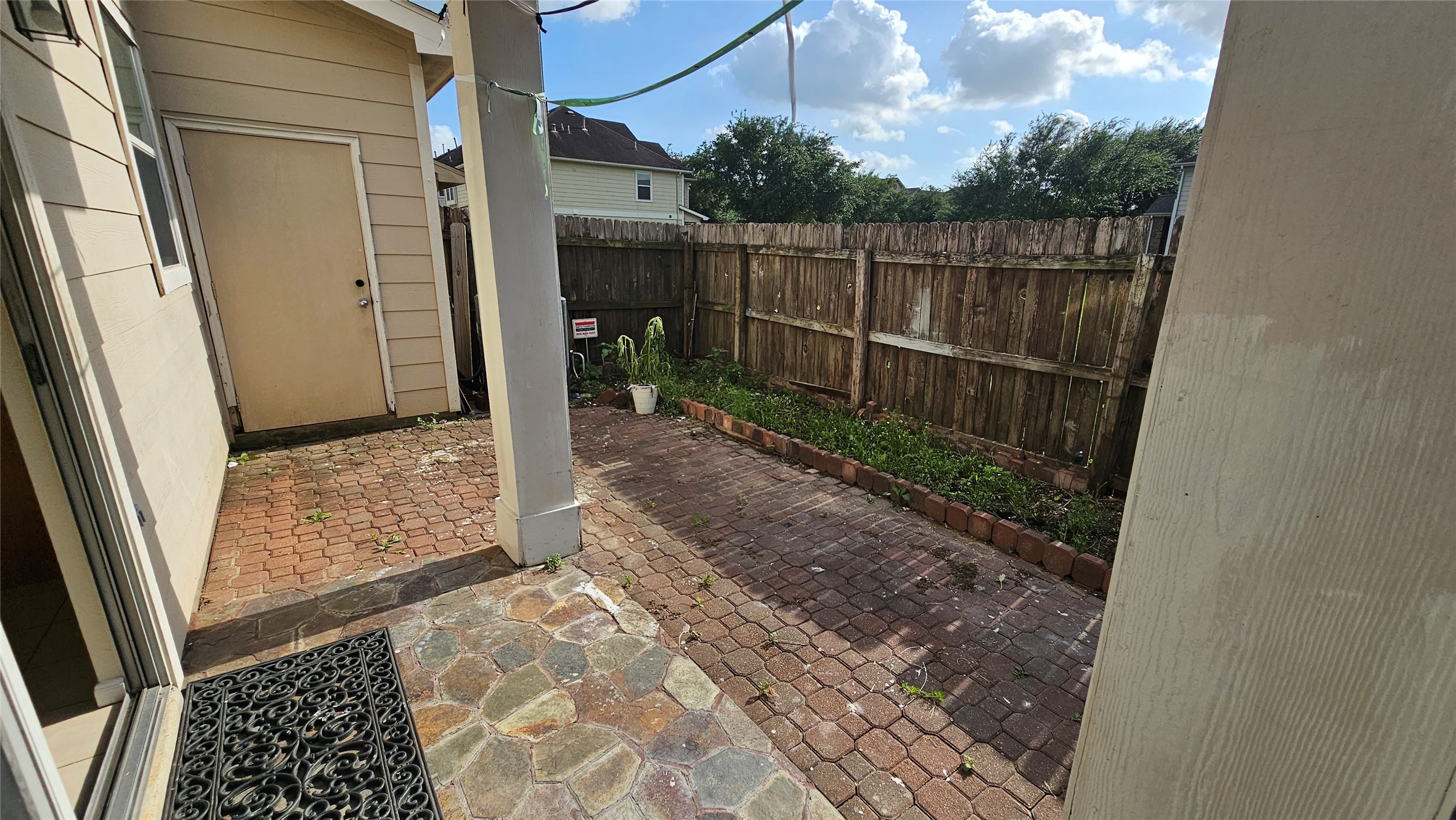 7918 Barnes Ridge Lane Houston, TX 77072 - Photo 31 of 34 Cozy backyard patio with a mix of stone and brick paving, bordered by a wooden fence. There's a small garden area along the fence, providing potential for landscaping or planting. Ideal for a private outdoor space.