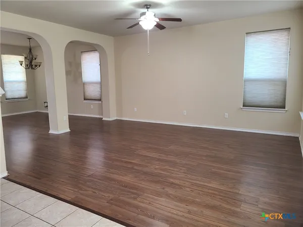 an empty room with wooden floor chandelier fan and windows