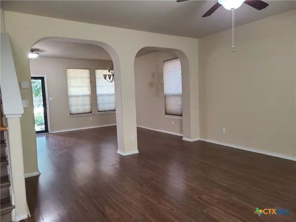 a view of an empty room with wooden floor and a chandelier fan