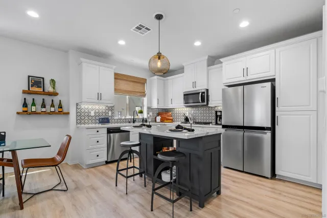 a kitchen with stainless steel appliances granite countertop a dining table chairs refrigerator and sink