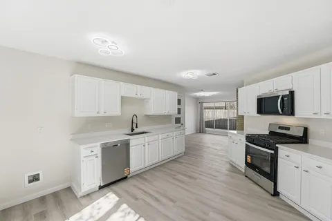 a large kitchen with stainless steel appliances a sink a stove top oven a counter space and cabinets