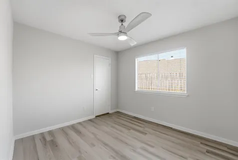 an empty room with wooden floor ceiling fan and windows
