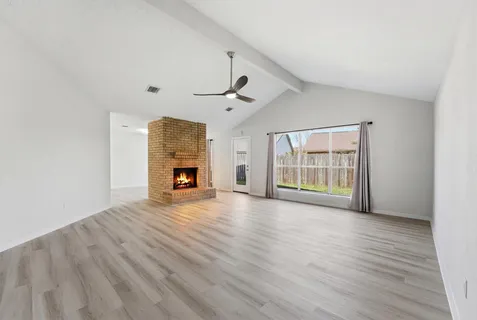 a view of an empty room with wooden floor fireplace and a window