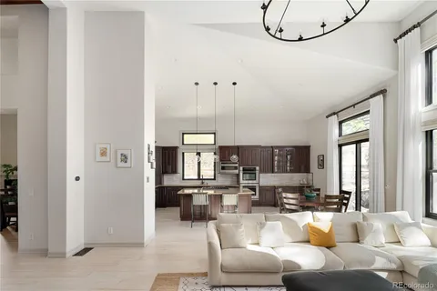 a living room with furniture a chandelier fan and kitchen view