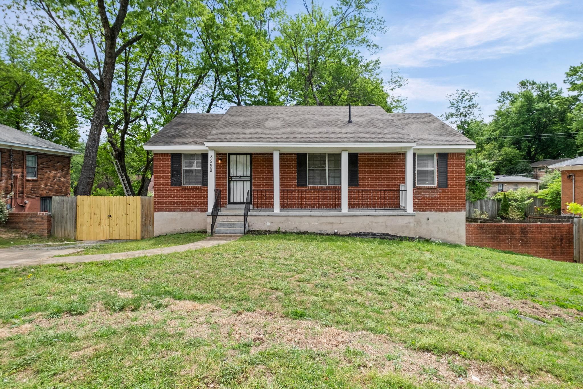 View of front of property featuring covered porch, brick siding, a gate, and a shingled roof