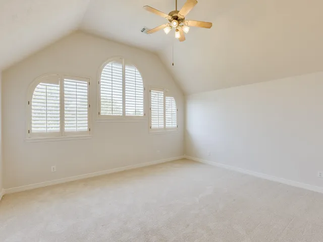 an empty room with a chandelier fan and windows