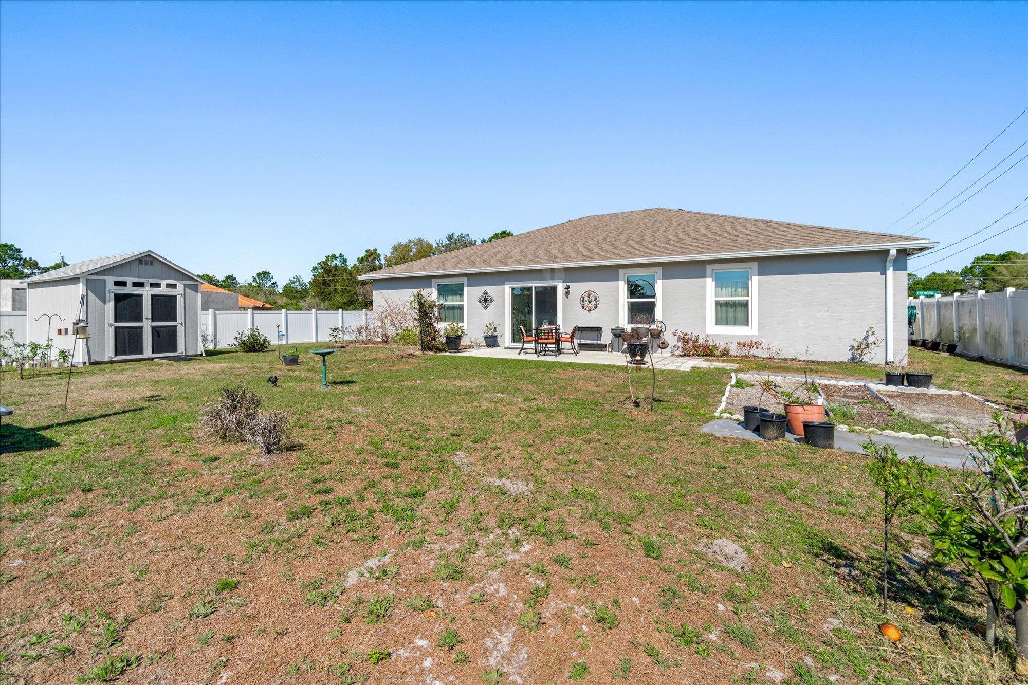 1 Frenora Lane Palm Coast, FL 32137 - Photo 27 of 43 Rear view of property featuring a fenced backyard, a patio, a storage shed, roof with shingles, and a vegetable garden