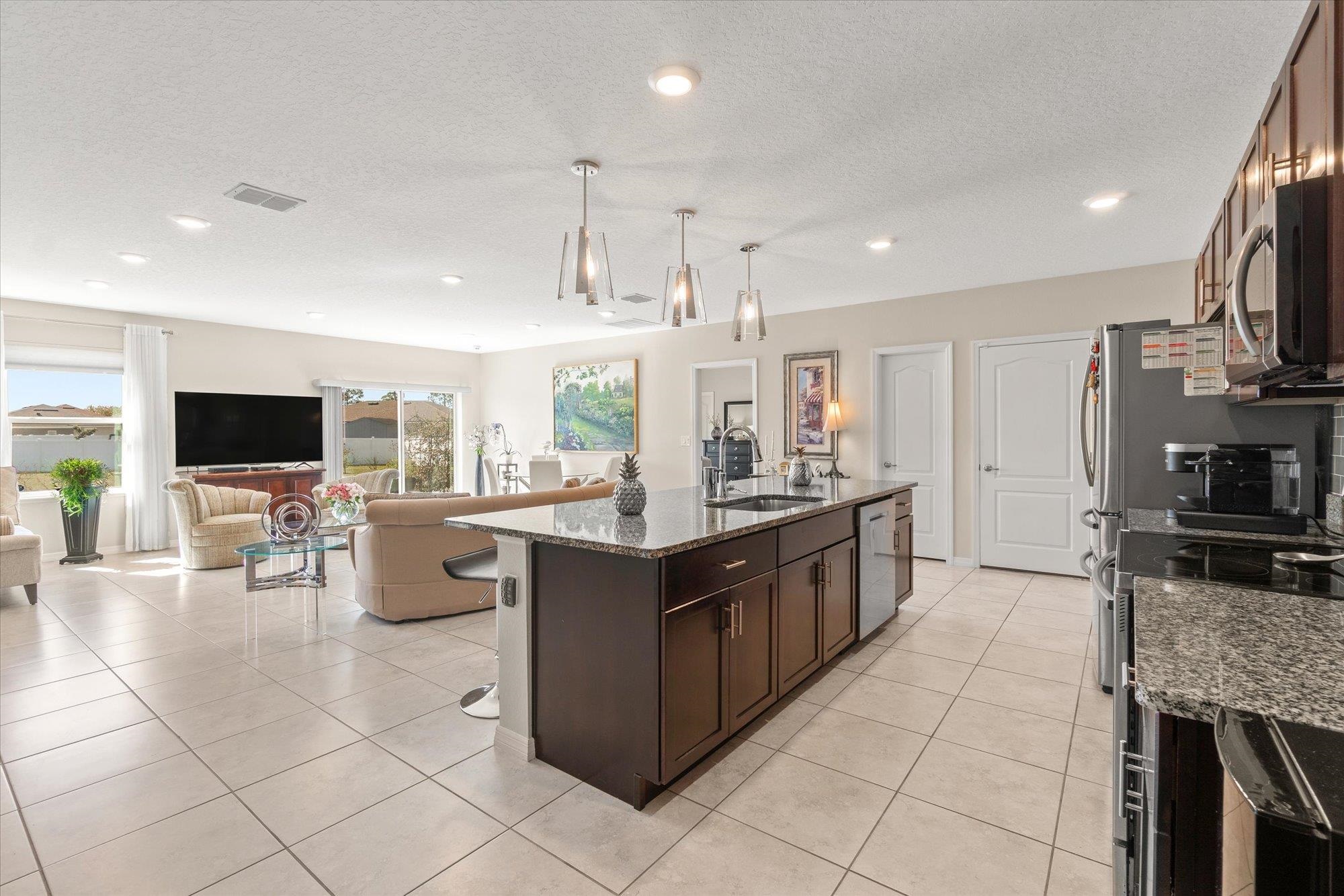 1 Frenora Lane Palm Coast, FL 32137 - Photo 42 of 43 Kitchen with dark wood finish cabinets, dark stone countertops, open floor plan, an island with sink, and hanging light fixtures