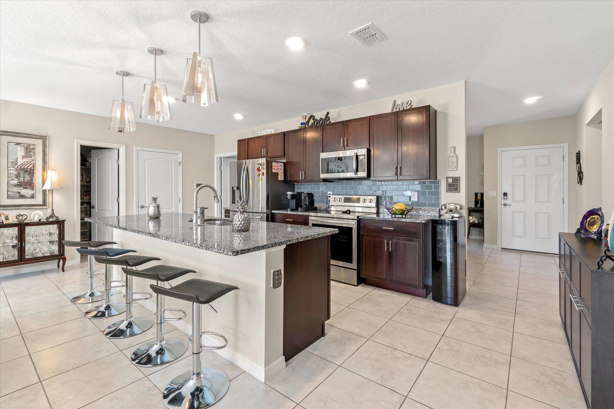 1 Frenora Lane Palm Coast, FL 32137 - Photo 5 of 43 Kitchen featuring a breakfast bar, stainless steel appliances, dark wood finish cabinets, light tile patterned floors, and a kitchen island with sink