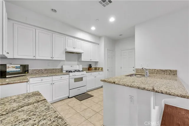 a kitchen with granite countertop sink stove and white cabinets with wooden floor
