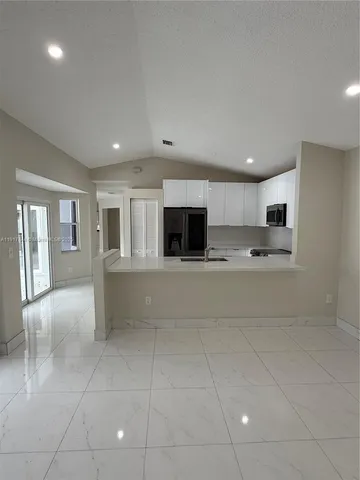 a large white kitchen with kitchen island granite countertop a refrigerator and a stove top oven