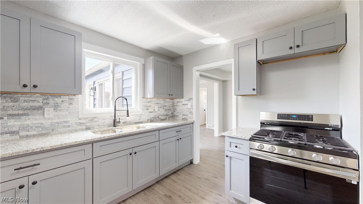 3932 Strandhill Road Cleveland, OH 44128 - Photo 19 of 27 Kitchen with light hardwood / wood-style flooring, stainless steel range with gas cooktop, a textured ceiling, tasteful backsplash, and sink