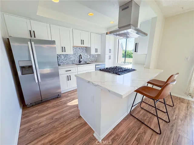 a kitchen with stainless steel appliances granite countertop a stove a refrigerator a sink a dining table and chairs with wooden floor