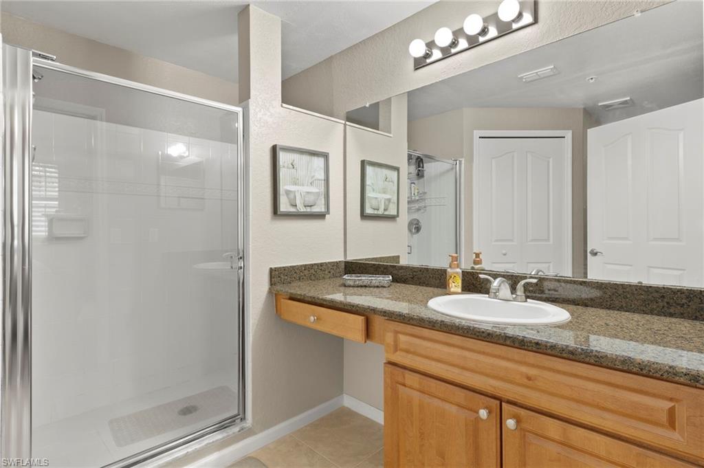 12955 Positano Circle, Unit 104 Naples, FL 34105 - Photo 20 of 40 a bathroom with a granite countertop sink a mirror and a shower
