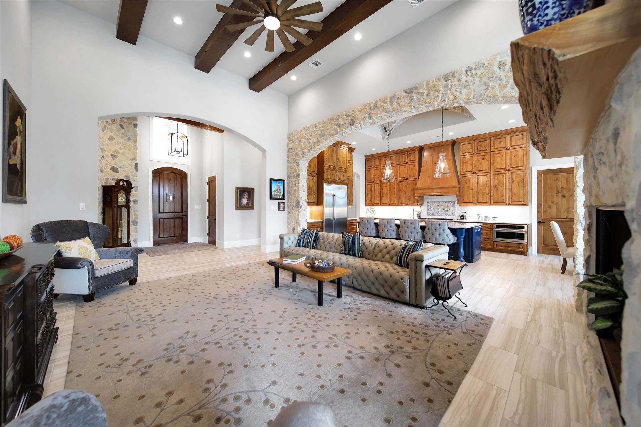 24718 Shadow Pond Spring, TX 77389 - Photo 10 of 49 Stunning open-concept living area featuring high ceilings with wooden beams, a cozy stone fireplace, and a seamless flow into the gourmet kitchen with rich wood cabinetry and a large island.