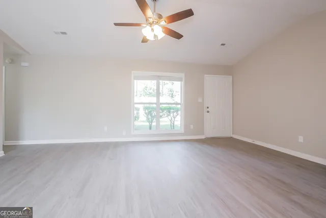an empty room with wooden floor fan and windows