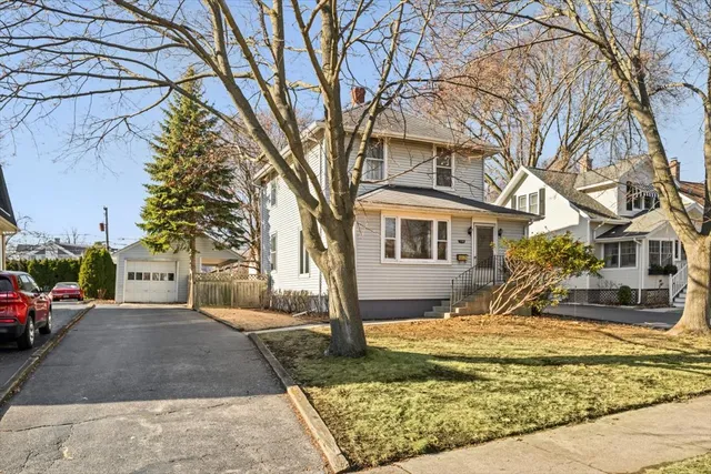 a view of a white house next to a yard with a fountain and large trees