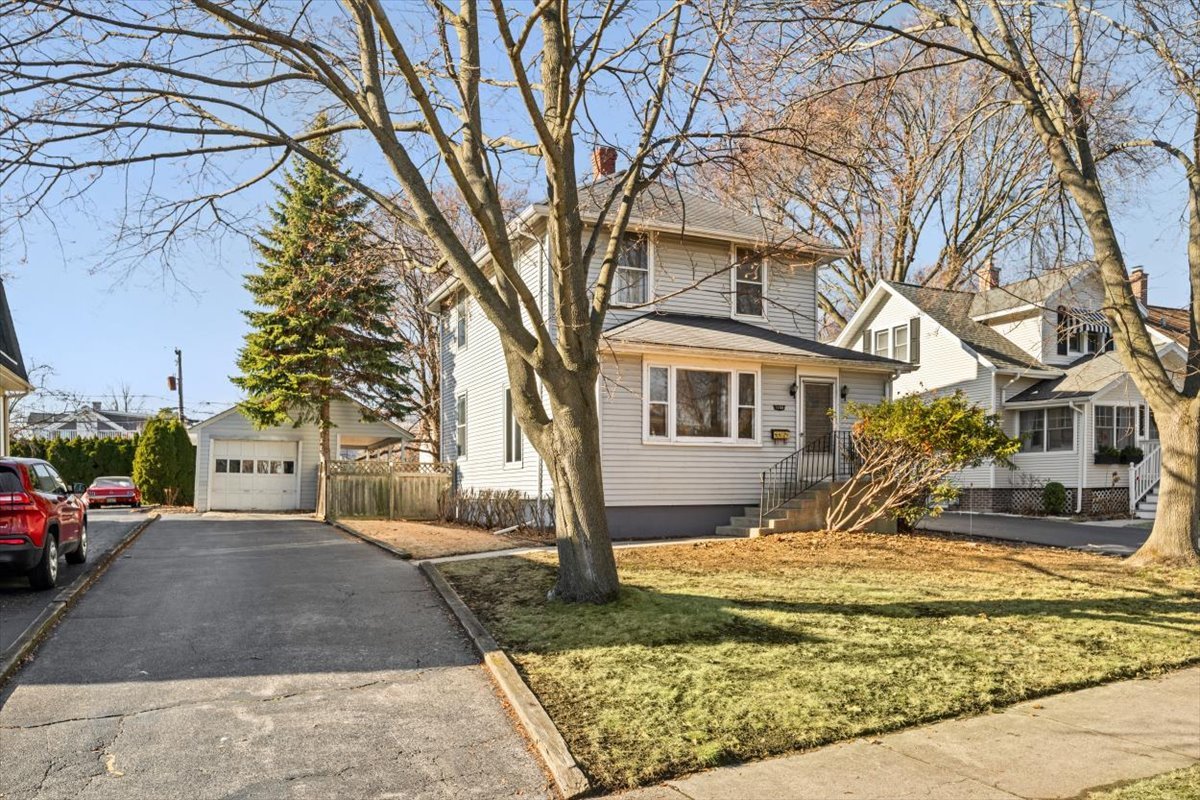 a view of a white house next to a yard with a fountain and large trees