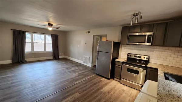 a kitchen with stainless steel appliances granite countertop a refrigerator a sink dishwasher a stove and a oven with wooden floor