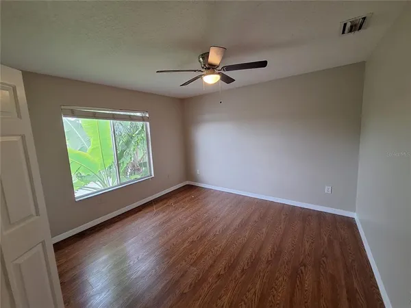 an empty room with wooden floor ceiling fan and windows