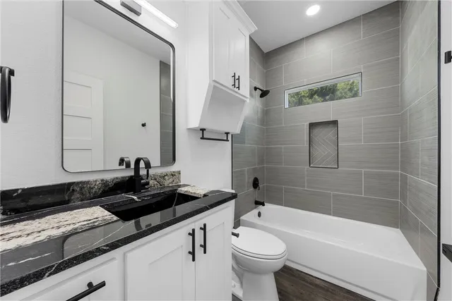 a bathroom with a granite countertop sink mirror bathtub and toilet