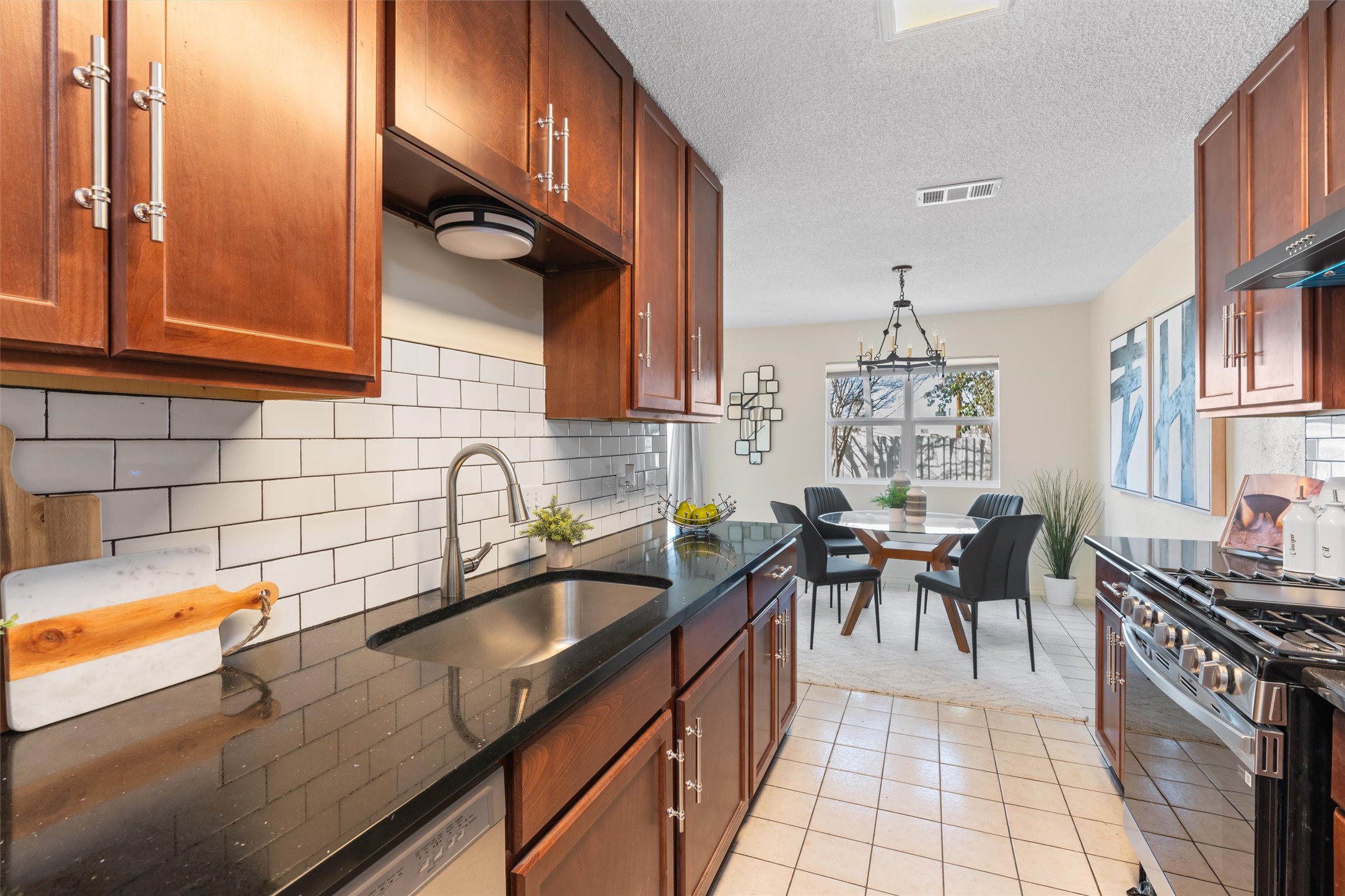11902 Barrington Way Austin, TX 78759 - Photo 11 of 30 Kitchen featuring stainless steel gas range oven, light tile patterned floors, dark stone counters, a textured ceiling, and hanging light fixtures