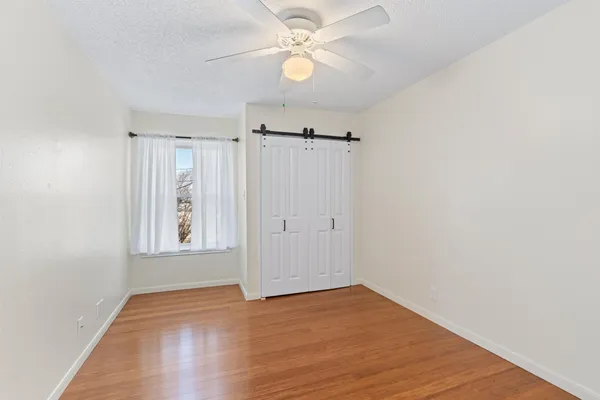 a view of an empty room with wooden floor and a ceiling fan