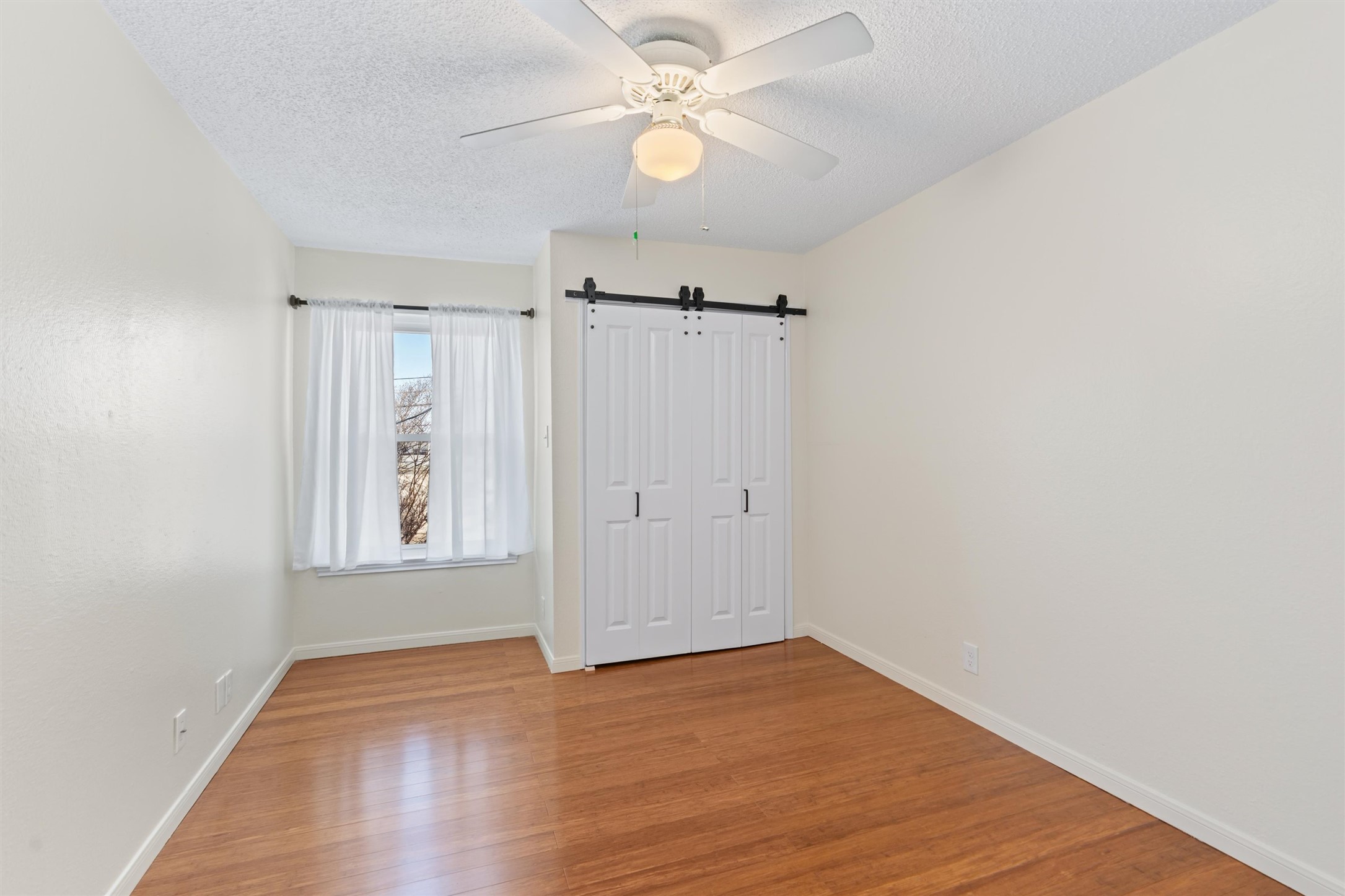 11902 Barrington Way Austin, TX 78759 - Photo 17 of 30 Second bedroom featuring a barn door, wood finished floors, a textured ceiling, ceiling fan, and a closet