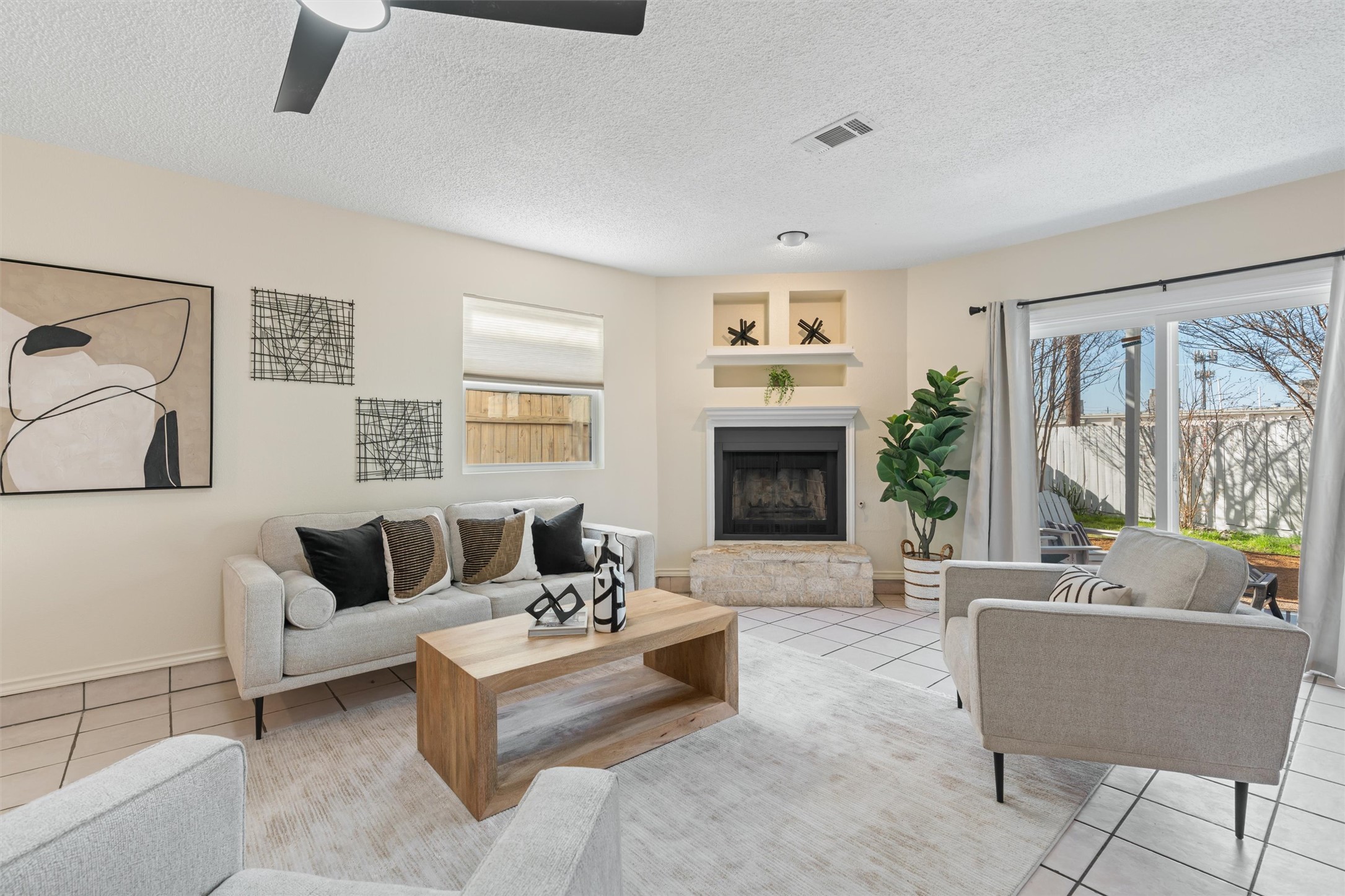 11902 Barrington Way Austin, TX 78759 - Photo 7 of 30 Living room featuring light tile patterned floors, a textured ceiling, a fireplace with raised hearth, and ceiling fan