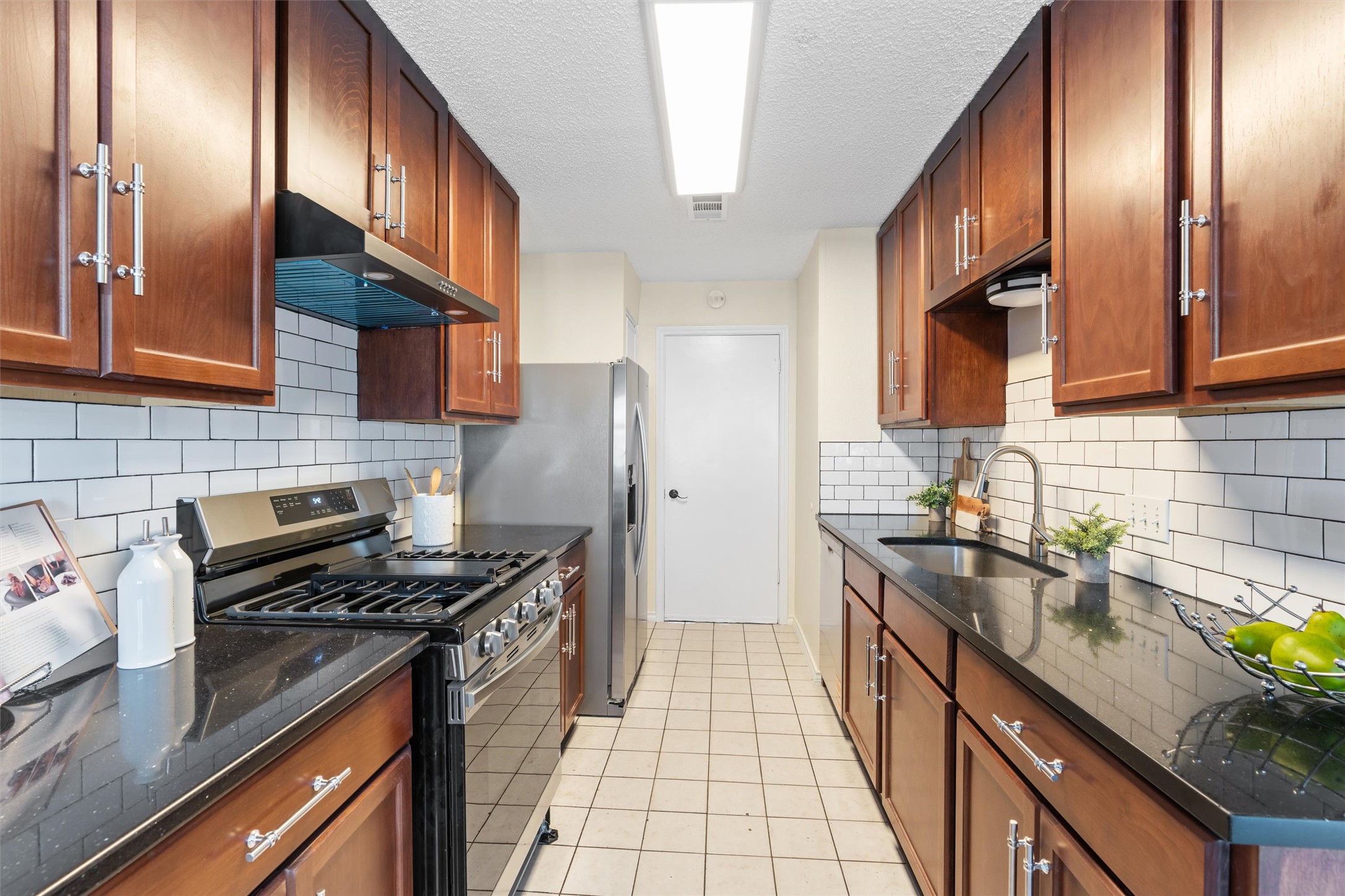 11902 Barrington Way Austin, TX 78759 - Photo 9 of 30 Kitchen with stainless steel appliances, dark stone counters, wood finish cabinets, a textured ceiling, and light tile patterned floors