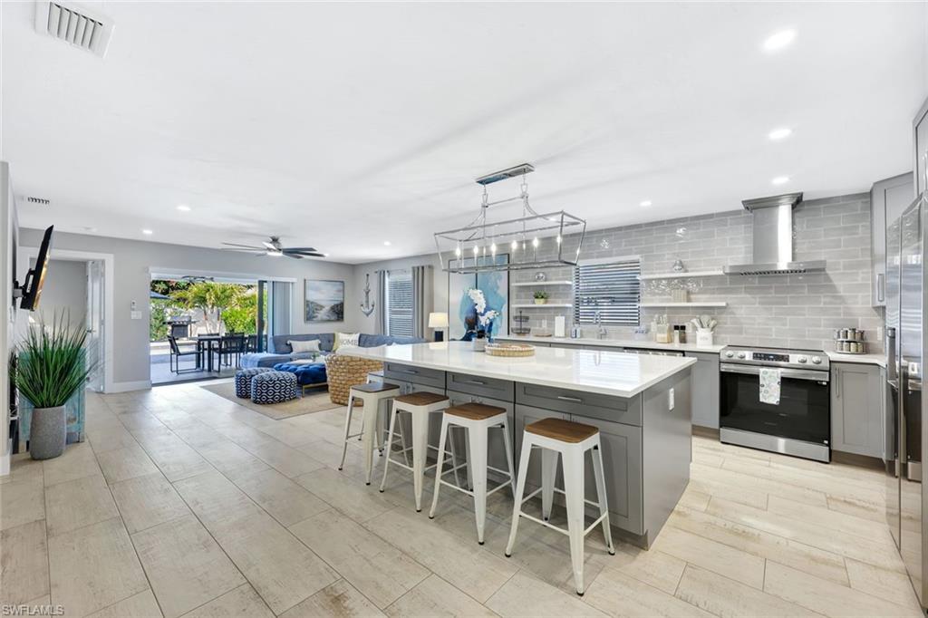 761 99th Avenue North Naples, FL 34108 - Photo 4 of 31 Kitchen with gray cabinetry, a breakfast bar, stainless steel appliances, tasteful backsplash, and open shelves