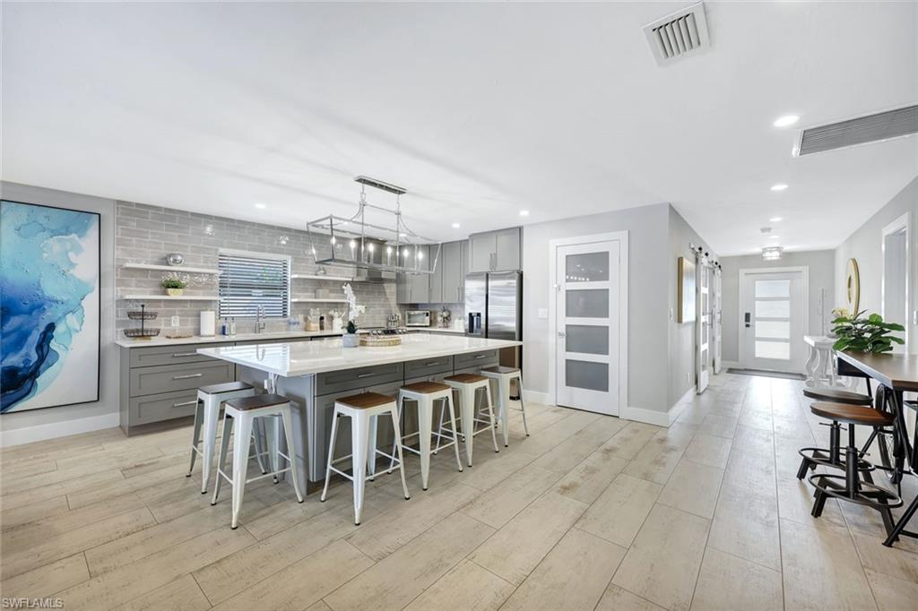 761 99th Avenue North Naples, FL 34108 - Photo 6 of 31 Kitchen featuring gray cabinets, a breakfast bar, decorative backsplash, light stone countertops, and a center island