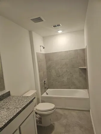 a bathroom with a granite countertop bathtub shower sink vanity and toilet