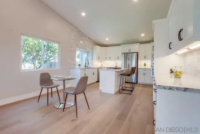 a kitchen with stainless steel appliances kitchen island granite countertop a dining table chairs and a refrigerator