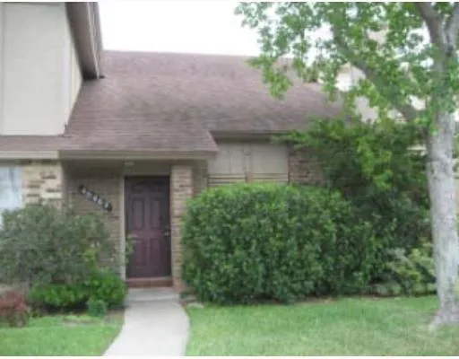 a view of brick house with a yard potted plants and large tree