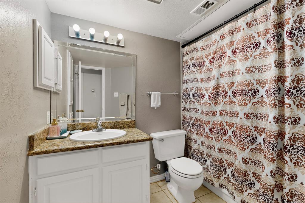 324 West Harwood Road, Unit A Hurst, TX 76054 - Photo 18 of 27 a bathroom with a granite countertop toilet a sink a mirror a lamp and a shower