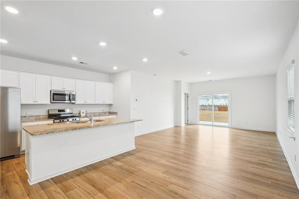 3853 Rustic Barn Way Loganville, GA 30052 - Photo 2 of 22 a large kitchen with stainless steel appliances granite countertop a stove a sink a refrigerator and white cabinets with wooden floor