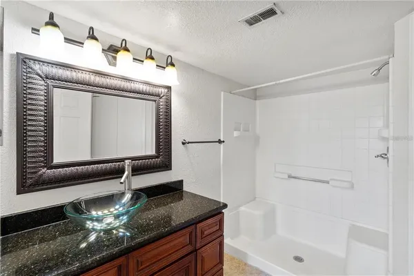 a bathroom with a granite countertop sink a mirror and shower