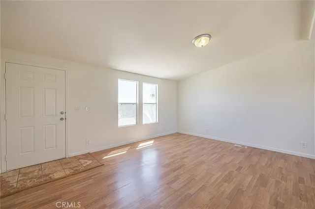 an empty room with wooden floor kitchen view and windows