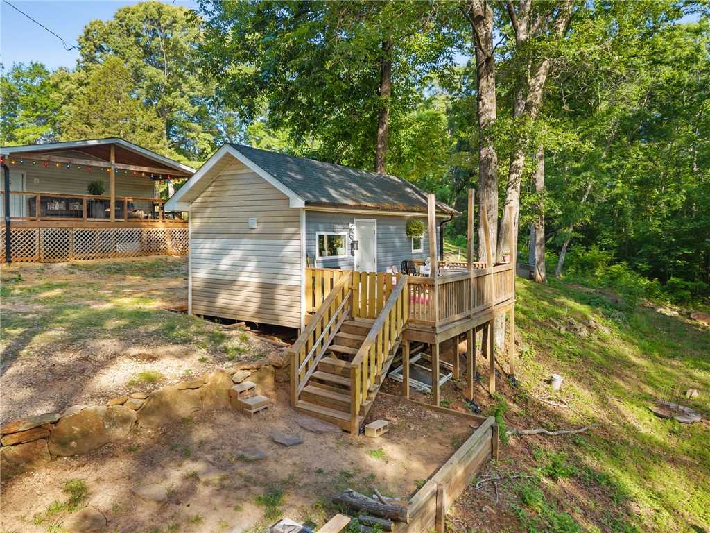 217 Old River Road Pelzer, SC 29669 - Photo 2 of 30 Perched among verdant trees, this property features a charming cottage with an elevated deck overlooking a natural, sloped landscape.