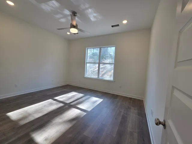 an empty room with wooden floor chandelier fan and windows
